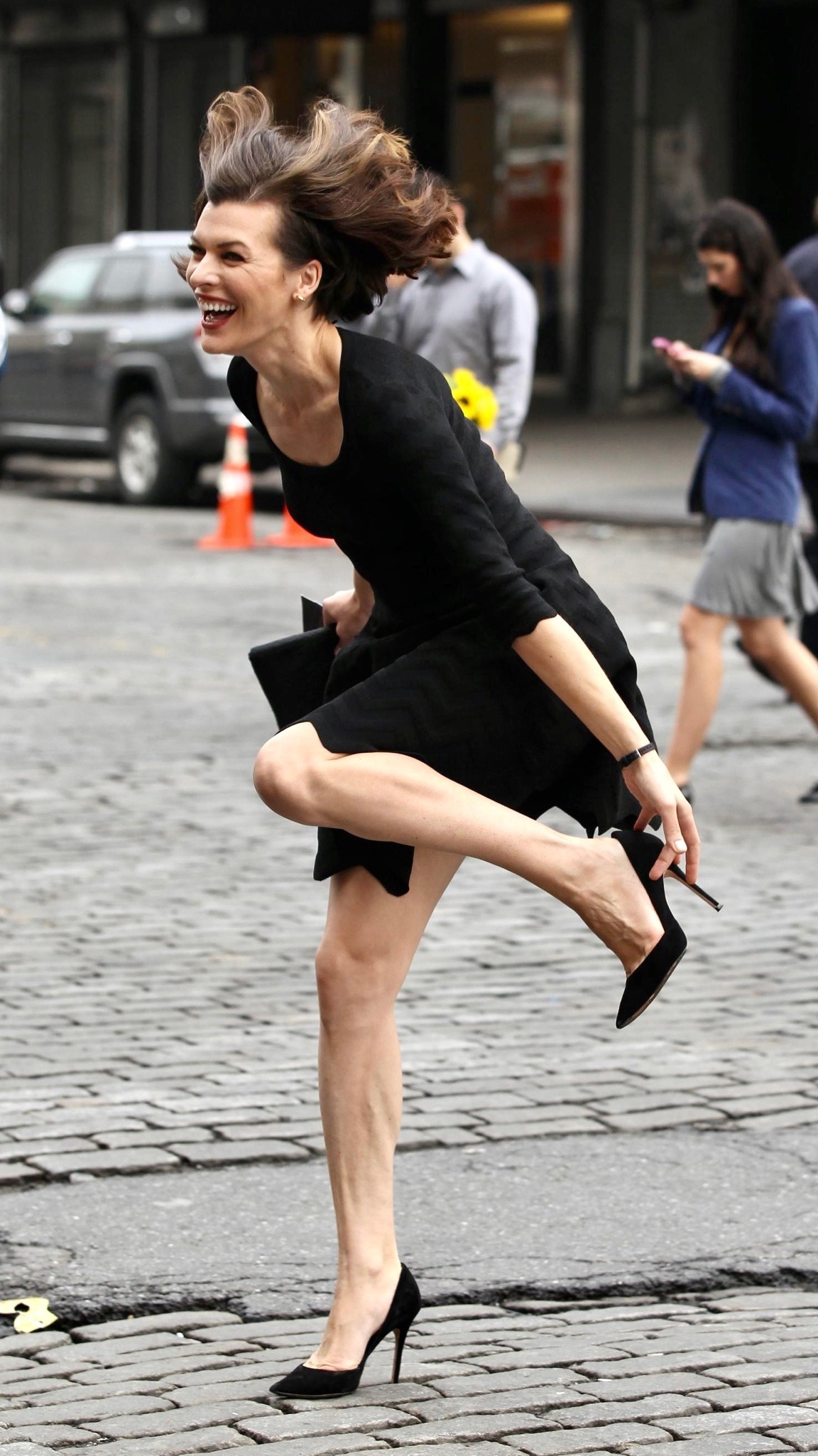 1152x2048, 440 Kb / Milla Jovovich, каблуки, брусчатка, платье, смех, улыбка, ветер, Милла Йовович